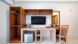 Una camera compatta con una scrivania in legno, televisore, forno a microonde, un piccolo frigorifero e una sedia.