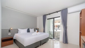 Una camera d'albergo moderna con un letto grande, un comodino in legno, una scrivania e un balcone con tavolo e sedie.