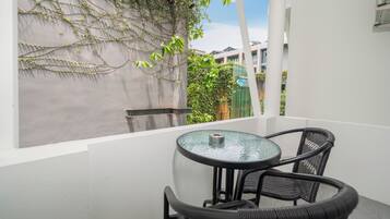 A glass-top table with wicker chairs in a white-walled room with a view of a building and greenery outside.