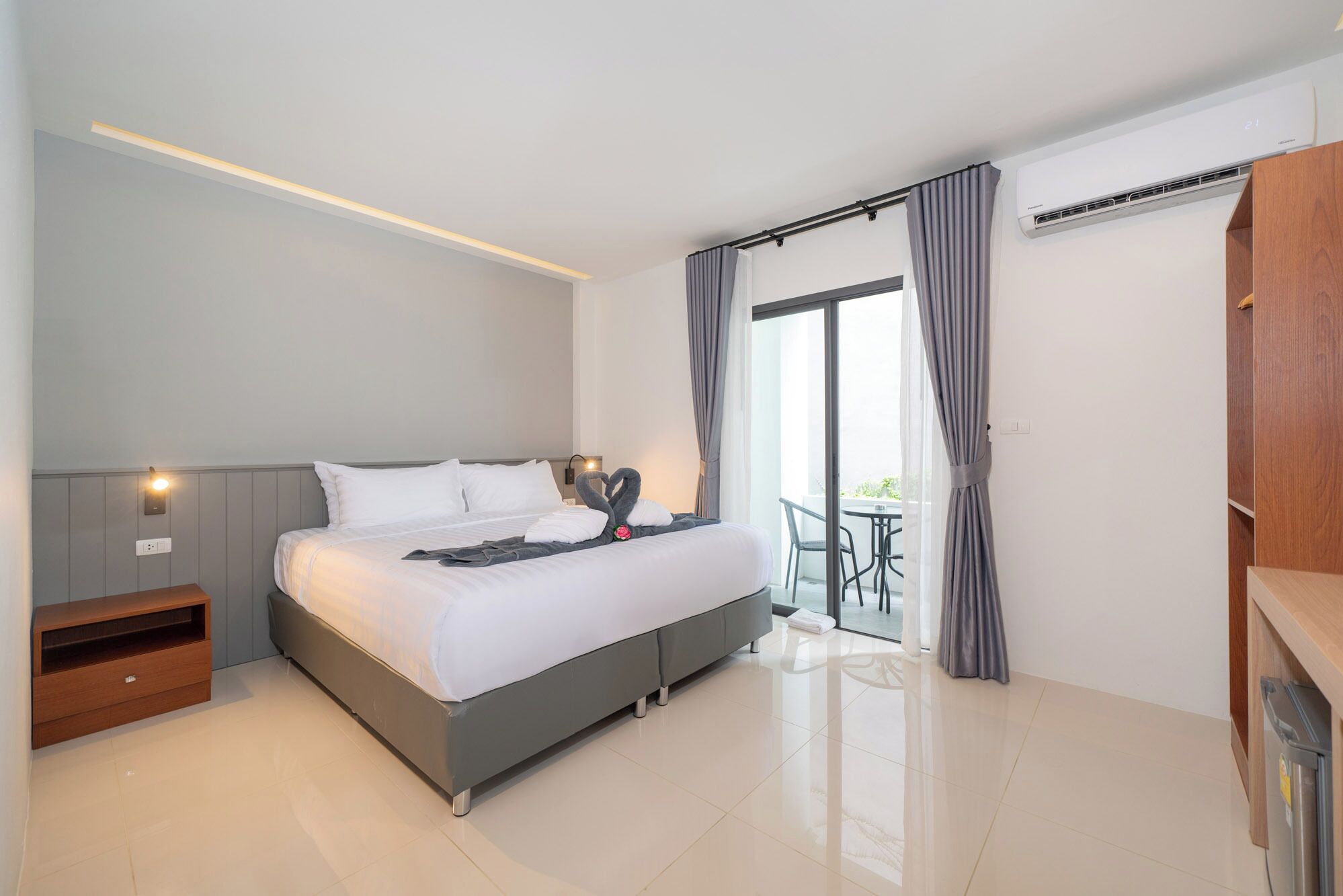 Ein modernes Hotelzimmer mit einem großen Bett, einem Nachttisch, einem Kleiderschrank und einem Balkon mit Tisch und Stühlen.