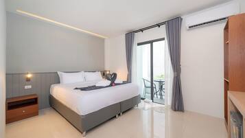 A modern hotel room with a large bed, a bedside table, a wardrobe, and a balcony with a table and chairs.