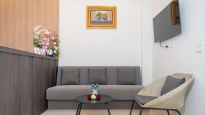 Un soggiorno moderno con un divano grigio, una poltrona in vimini, un tavolino rotondo con una sveglia e un quadro incorniciato appeso al muro.