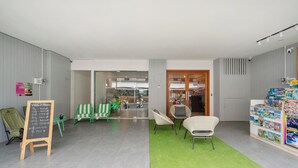 Un interno moderno con tappeto verde, sedie in vimini, un menu scritto alla lavagna e una vetrina con libri per bambini.