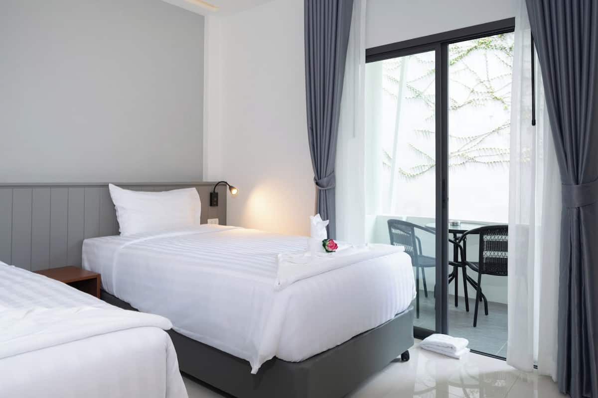 A hotel room with two beds, a nightstand, a bedside lamp, a small table with chairs, and a sliding glass door leading to an outdoor area.