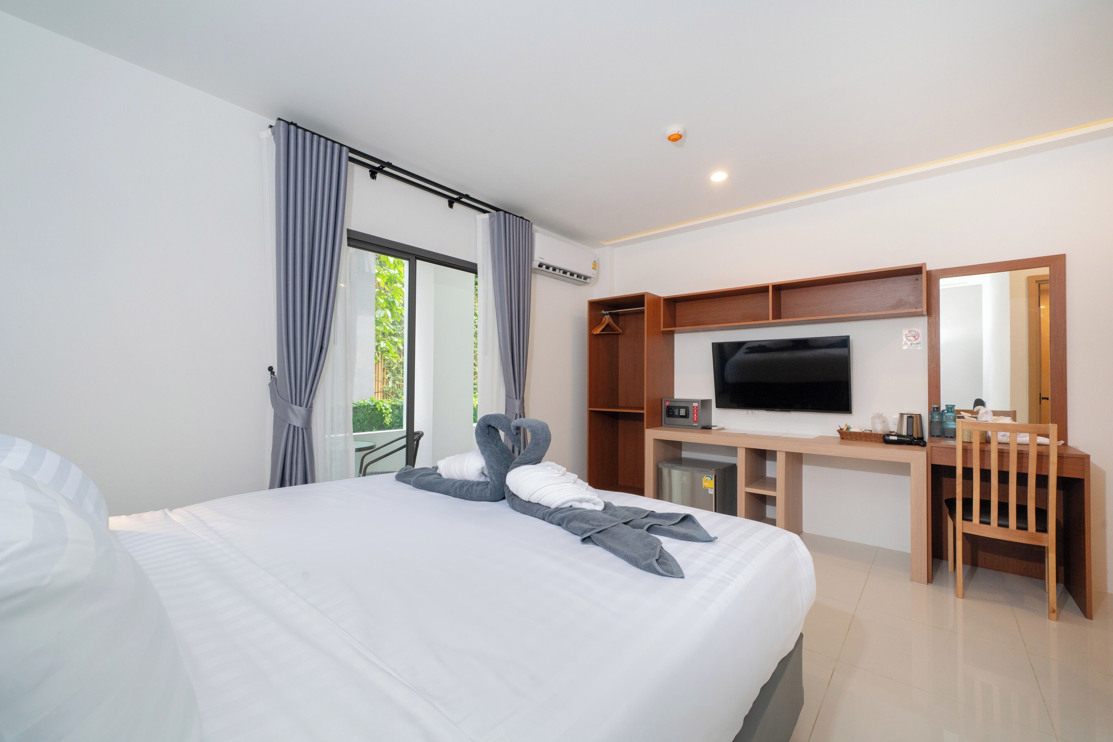 A modern hotel room with a large bed, a desk with a flat-screen TV, a chair, and a wardrobe.