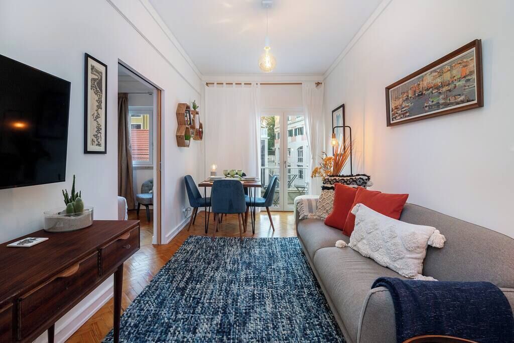 Una sala moderna con un sofá, una mesa de centro y un televisor sobre un mueble bajo. Hay un comedor con una mesa y sillas.