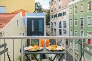 Un balcón con alimentos para el desayuno y un vaso de jugo de naranja.
