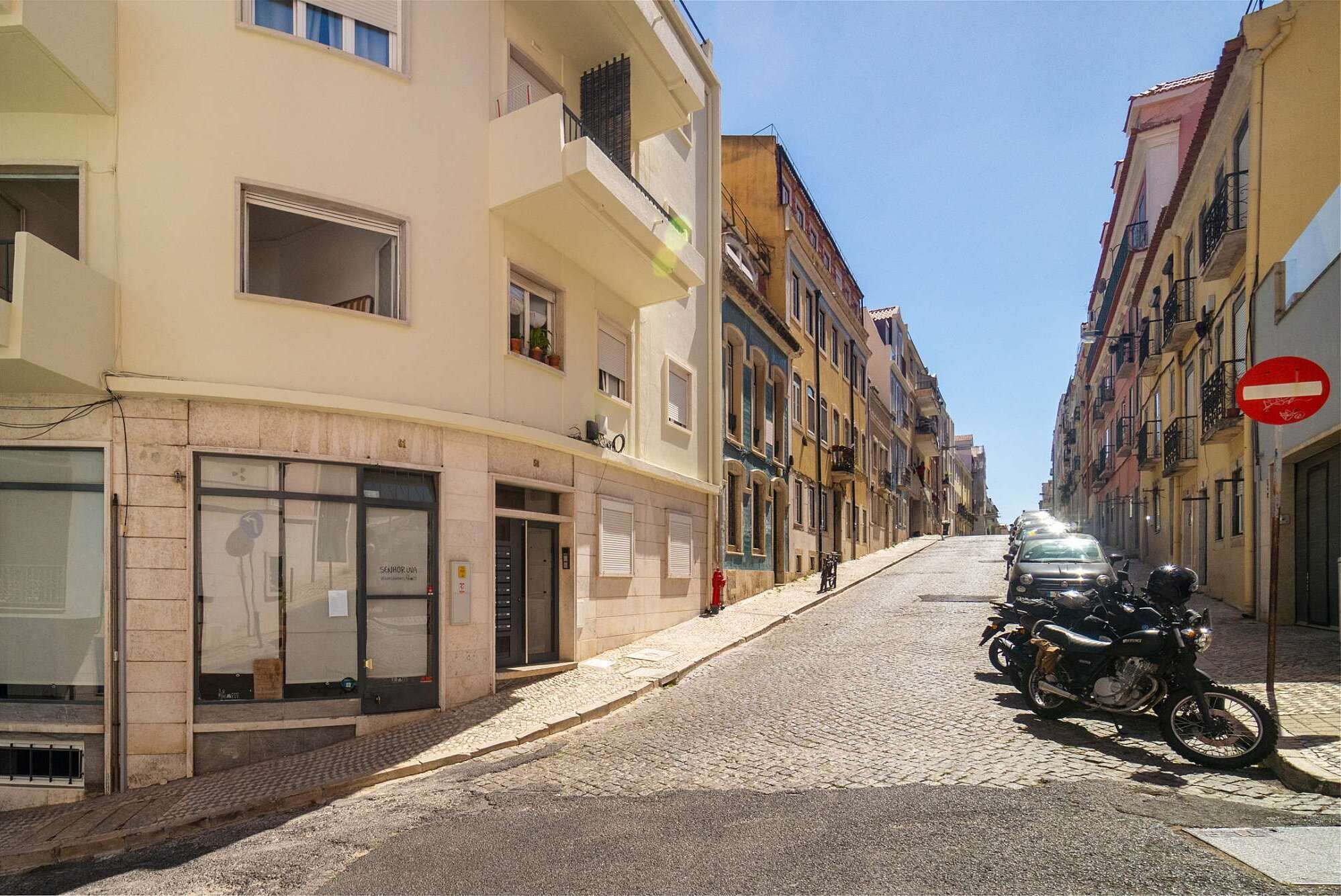 A cobblestone street lined with multi-story buildings, a parked motorcycle, and a 'no entry' sign.
