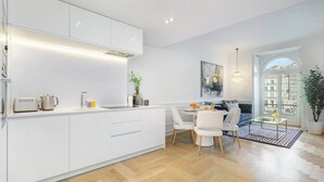 Una cucina moderna con mobili bianchi, un'area pranzo con tavolo in vetro e vista sugli edifici attraverso un'ampia finestra.