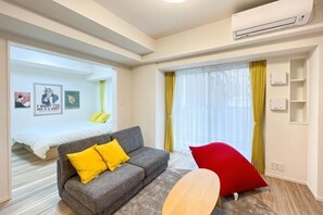 A hotel room with a sofa, a red chair, a bed, a window with curtains, and an air conditioning unit. - Park Axis Honjo Azumabashi South Residence (Tokyo)