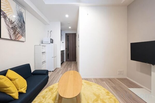 Un salon moderne avec un canapé, une table basse, un téléviseur à écran plat et une cuisine en arrière-plan.