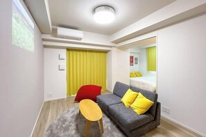 A modern hotel room with a grey sofa, yellow cushions, a wooden bench, a large mirror, and a yellow curtain. - Park Axis Honjo Azumabashi South Residence (Tokyo)