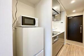 Une cuisine compacte avec un four à micro-ondes posé sur le dessus d’un réfrigérateur blanc, un évier et une porte sombre.