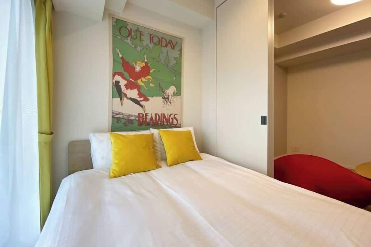 Habitació d'hotel amb un llit, dos coixins grocs, una cadira vermella i un cartell a la paret.