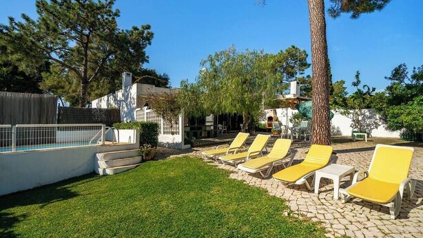 Un patio trasero con piscina, sillas de descanso amarillas y una cerca blanca.
