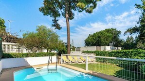 Una piscina con una escalera de metal, rodeada por una valla blanca y sillas de descanso amarillas.