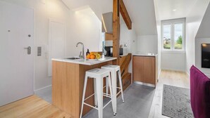 A modern kitchen with a central island, wooden beams, and a view of the outdoors.