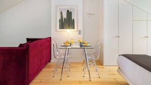 A compact room with a dining table set for two, a red sofa, a bed, and a white wardrobe.