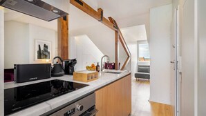 A modern kitchen with a built-in stove, oven, and sink. There is a wooden island with a cutting board and fruits. A staircase leads to a balcony with a view.
