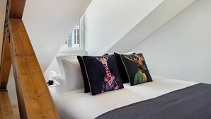 Ein Schlafzimmer mit schräg stehender Decke, einem Bett mit weißer Bettwäsche und zwei dekorativen Kissen mit Tiermotiven.