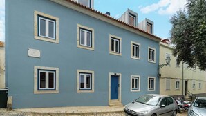 Ein zweistöckiges Gebäude mit blauer Fassade, zahlreichen Fenstern und einer blauen Tür. Autos sind vor dem Gebäude geparkt.
