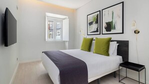 Ein modernes Schlafzimmer mit Bett, Nachttisch, Fernseher und zwei gerahmten Kunstwerken an der Wand.