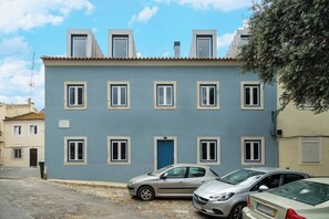 Un edificio de dos pisos con fachada azul, múltiples ventanas y una puerta también azul. Hay dos coches estacionados adelante.