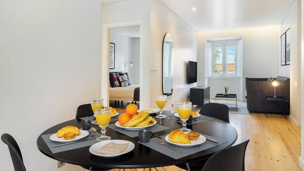 Ein moderner Essbereich mit einem runden Tisch, gedeckt für ein Frühstück, inklusive Croissants, Obst und Orangensaft.
