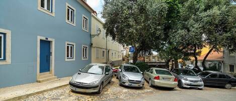 Una fila de autos estacionados a lo largo de una calle empedrada, flanqueada por edificios.