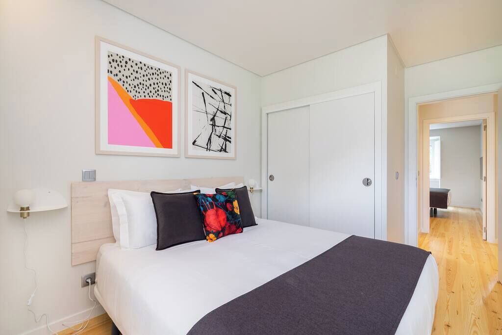 A modern hotel room with a large bed, white walls, and two abstract paintings.