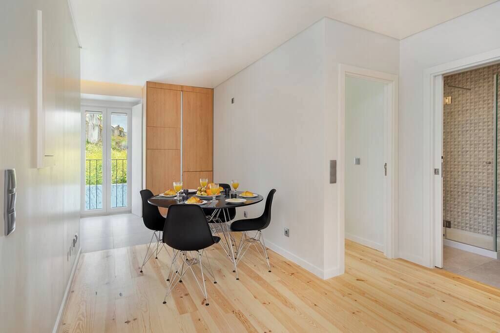 A modern dining area with a wooden cabinet, a table set with plates and glasses, and black chairs.