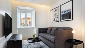 Ein modernes Wohnzimmer mit einem grauen Sofa, einem schwarzen Couchtisch, einem Fernseher und Kunstwerken an der Wand.