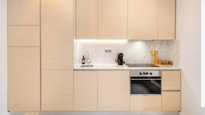 A modern kitchen with light wood cabinetry, a white countertop, a built-in oven, and a coffee maker. - Lisbon Prime Aparts - BeatoHub (Lisboa)