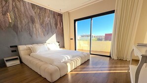 Une chambre moderne avec un grand lit, une porte-fenêtre coulissante donnant sur un balcon et une vue sur le paysage urbain.