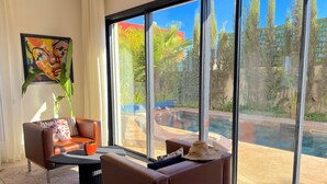 Un salon moderne avec une grande fenêtre, un tableau et une vue sur une piscine et un espace verdoyant.