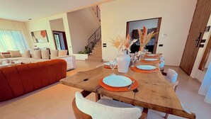 Un coin repas avec une table en bois dressée pour six personnes, entourée de chaises dotées de coussins blancs.