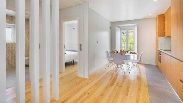 Une cuisine moderne avec des meubles en bois, un coin repas doté d’une table et de chaises blanches, et une grande fenêtre qui laisse entrer la lumière naturelle.