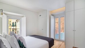 Une chambre à coucher avec un lit, des murs blancs, un plancher en bois et une vue sur un balcon.