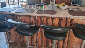 A kitchen counter with bar stools, jars of condiments, a kettle, and a microwave. - elephant memories safari lodge (marloth park)