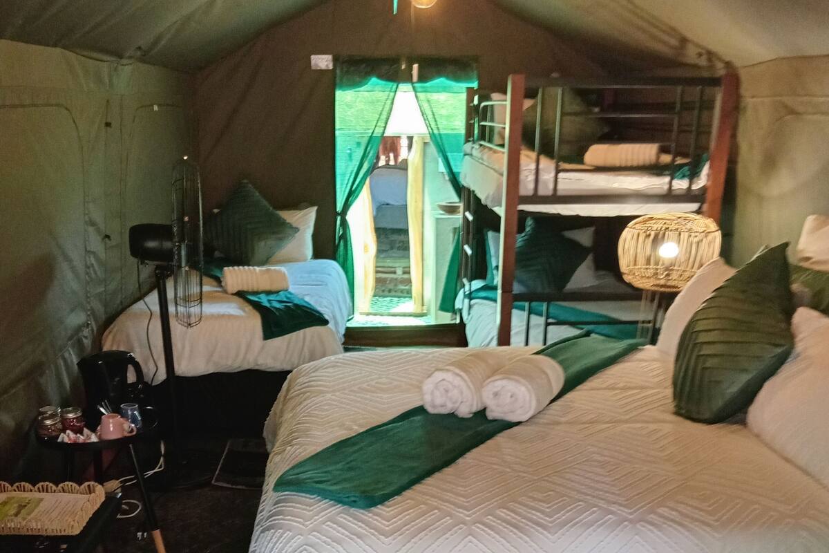 A tented room with two beds, a table with a basket, a chair, and a hanging light fixture.