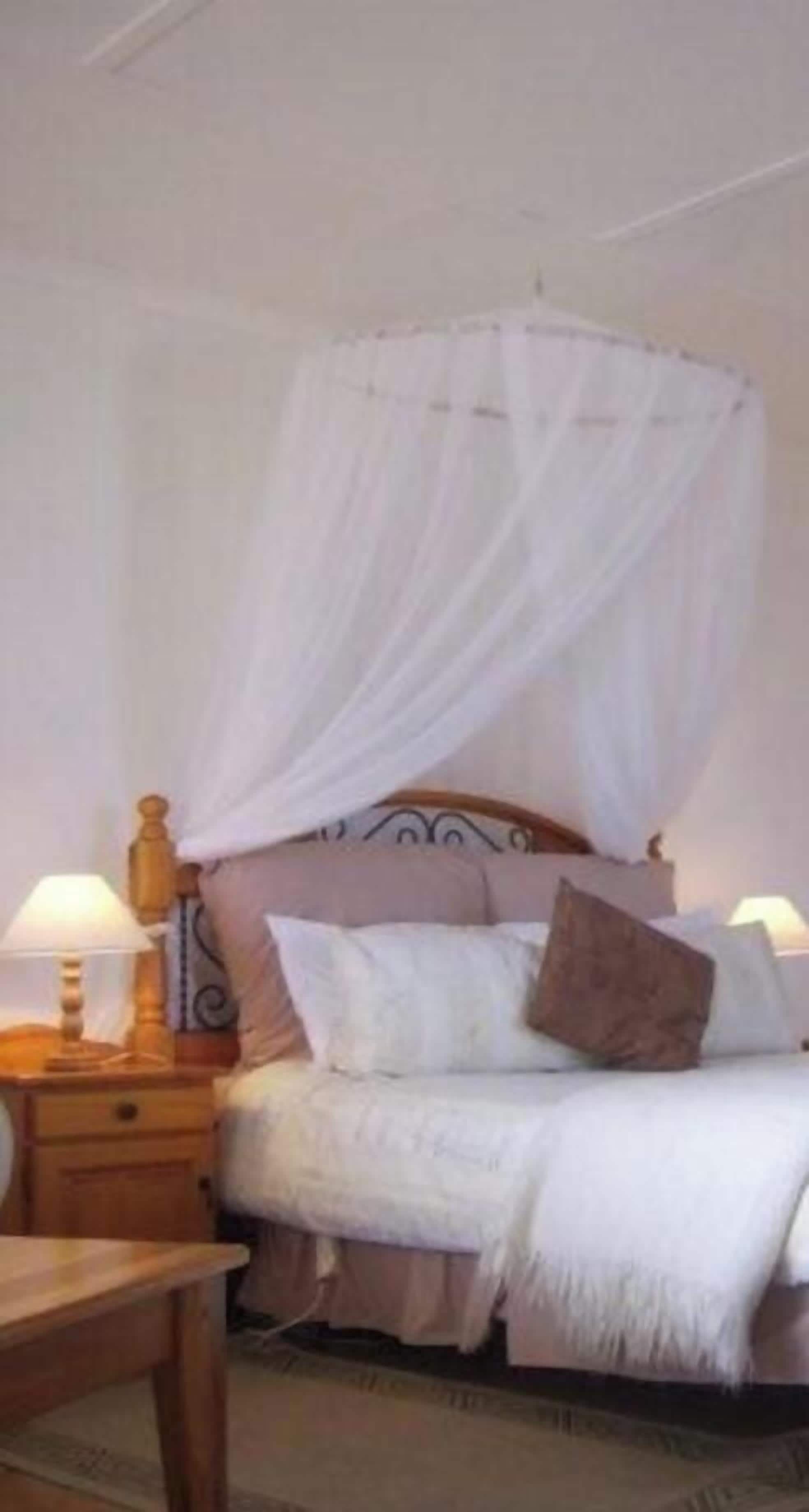 A bedroom with a canopy bed, bedside lamps, and a wooden nightstand.