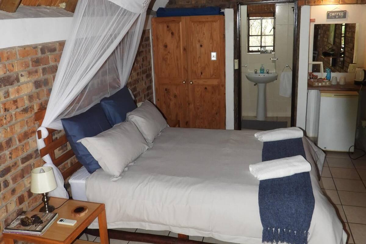 A bedroom with a bed, a nightstand, a wooden wardrobe, and a bathroom visible through an open door.