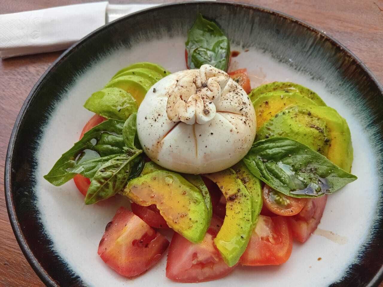 Une assiette avec un œuf poché, des tomates et du basilic.