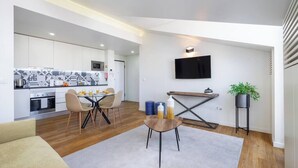 A modern kitchen with white cabinets, a dining area with a table and chairs, a TV mounted on the wall, and a potted plant. - Alcântara Premium 2-bed | Wi-Fi | Lx Factory (Lisboa)