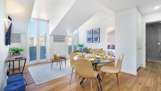A modern dining area with a round table, chairs, and a view of the city through large windows. - Alcântara Premium 2-bed | Wi-Fi | Lx Factory (Lisboa)