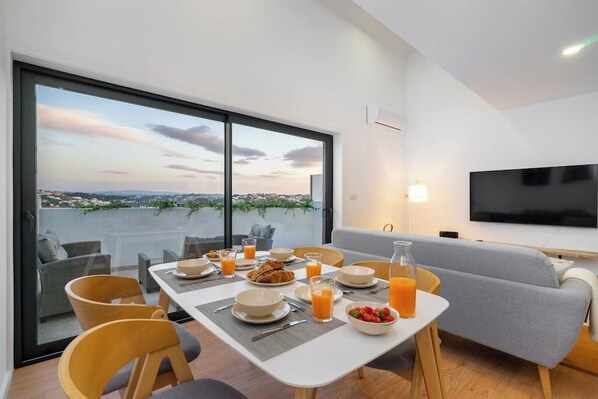 Et moderne spiseområde med et bord dækket til morgenmad, en sofa og et fjernsyn.