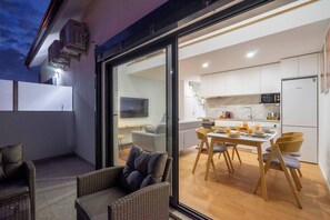 Et moderne køkken med hvide skabe, en mikrobølgeovn og et køleskab. Der er et spiseområde med et bord og stole, samt en balkon med fletmøbler.