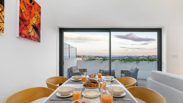 A dining area with a table set for breakfast, a city view through large windows, and a modern interior design.