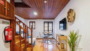 Een kamer met houten vloer, een wenteltrap, een eettafel met stoelen, een brandblusser en een wandmand.