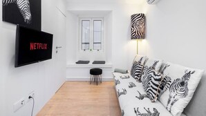 A modern living room with a white sofa, zebra-patterned cushions, a mounted TV, and a zebra-themed wall lamp.